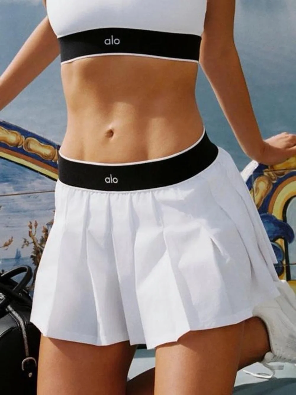 alo Yoga Low Rise AMP It Up Tennis Skirt in White with Black Waistband. SIZE: S